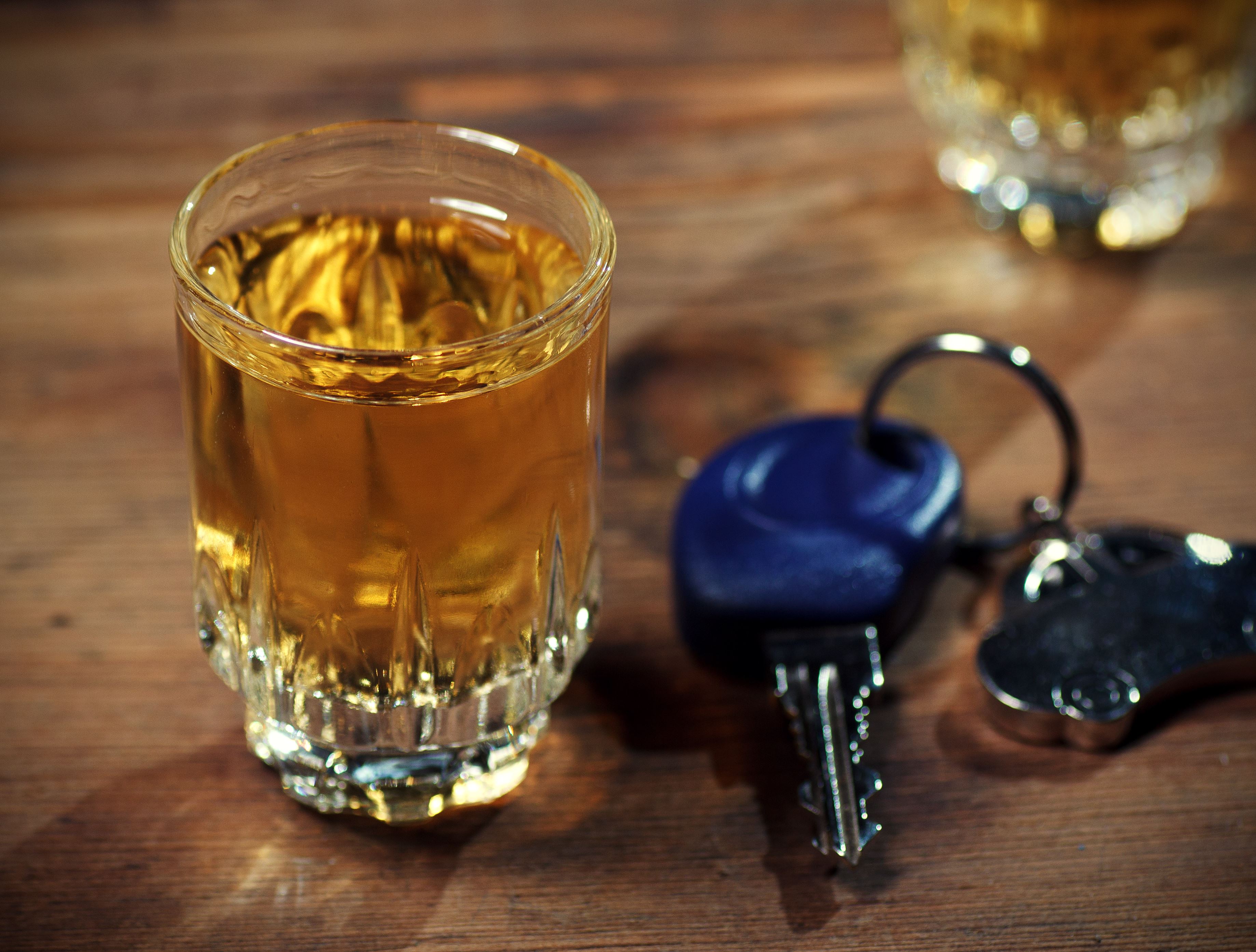 A shot of whiskey on a wooden table next to car keys